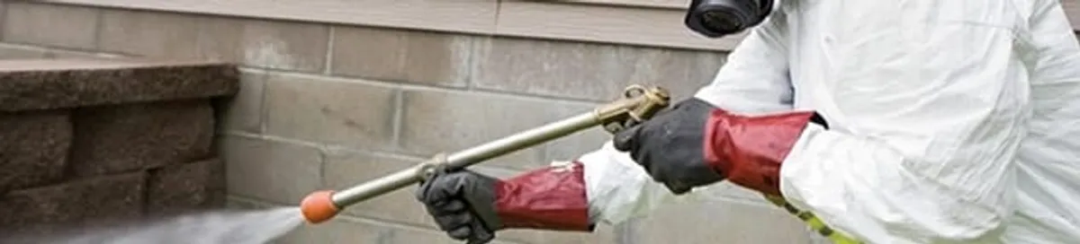 Pest control technician applying exterior insect treatment along a home foundation in Tacoma, WA