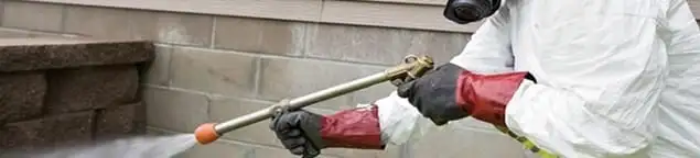 Pest control technician applying exterior insect treatment along a home foundation in Tacoma, WA
