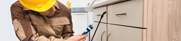 Roach exterminator applying treatment under kitchen cabinets in Tacoma, WA