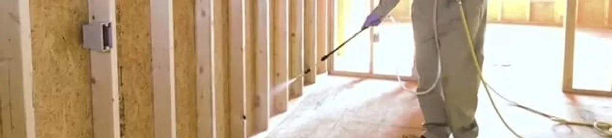Termite treatment technician applying spray along framing and unfinished walls in Tacoma, WA